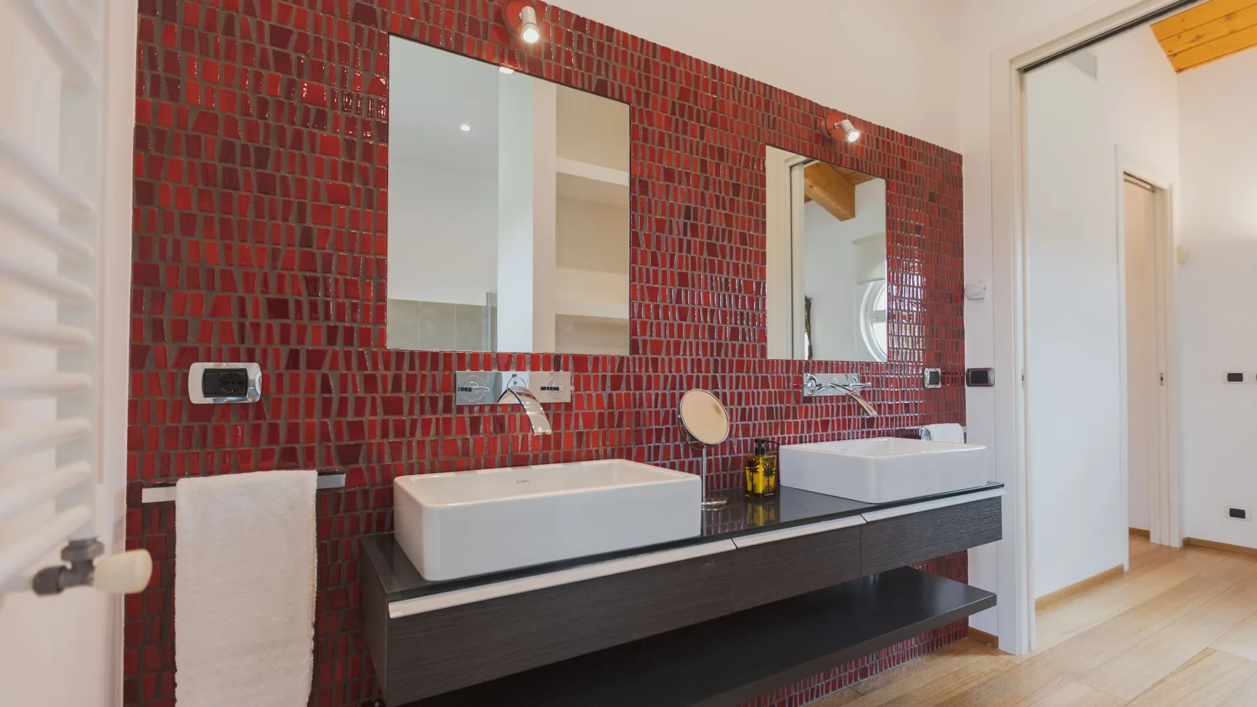 Un baño con dos lavabos y espejos frente a una pared de azulejos rojos.