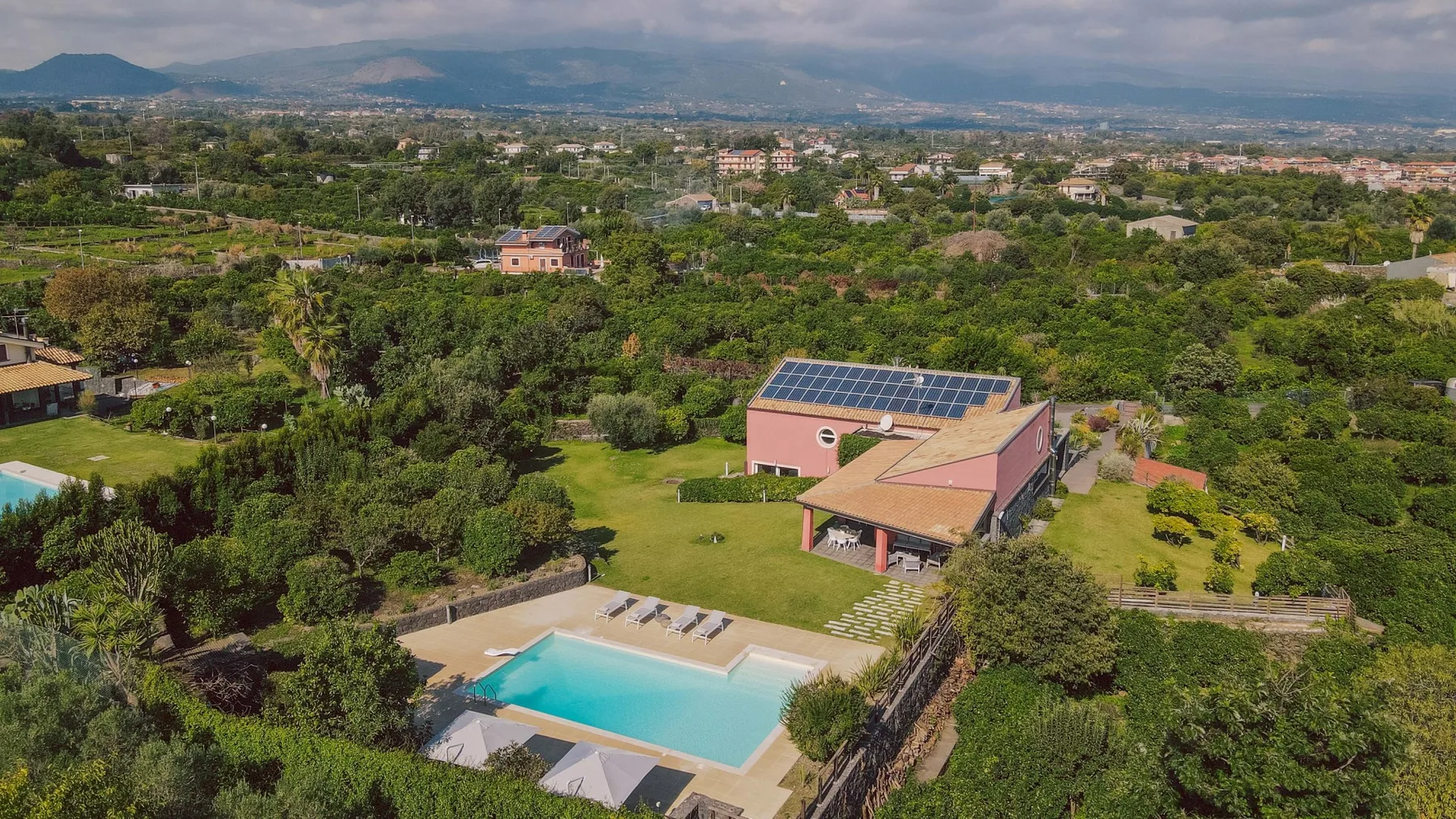 Una vista aérea muestra una piscina junto a una casa entre zonas verdes.