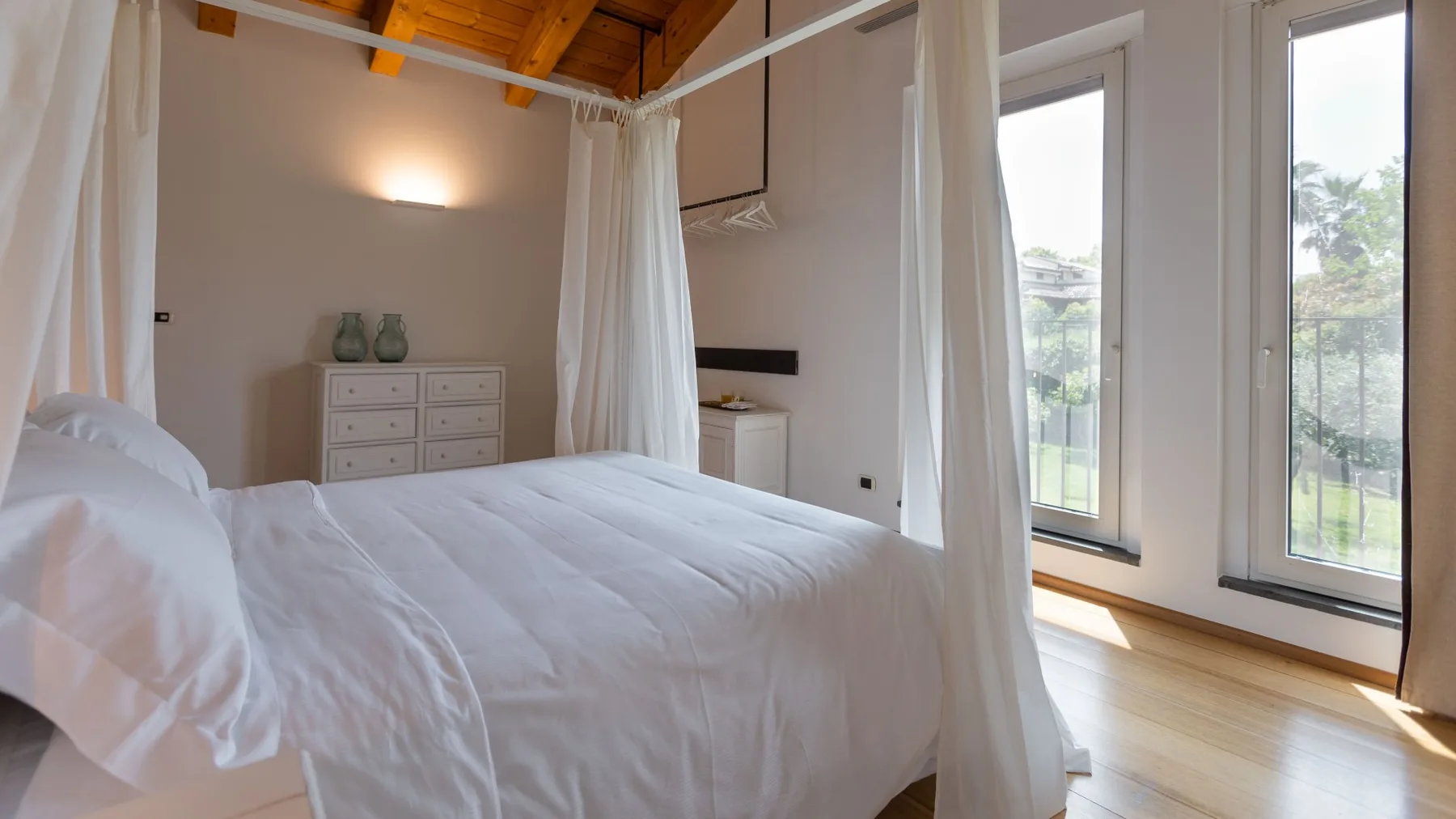Un dormitorio luminoso con una cama blanca y ventanas altas.