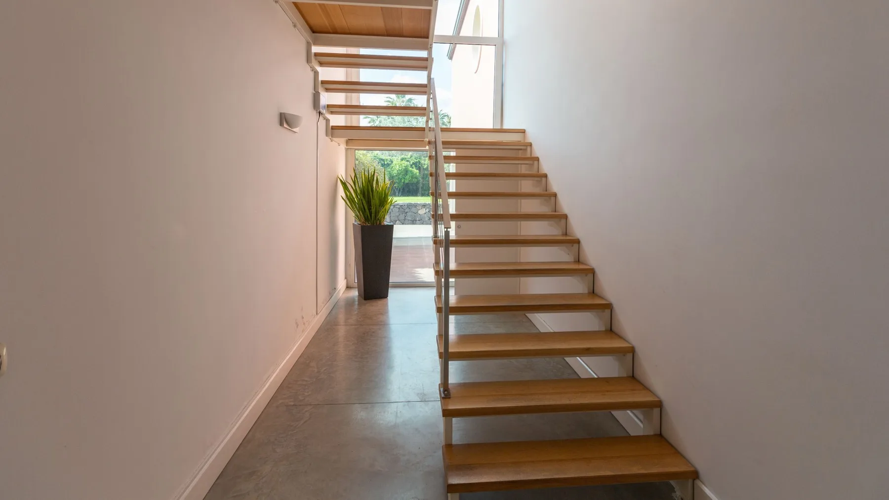 Una escalera luminosa con peldaños de madera y barandilla de vidrio.