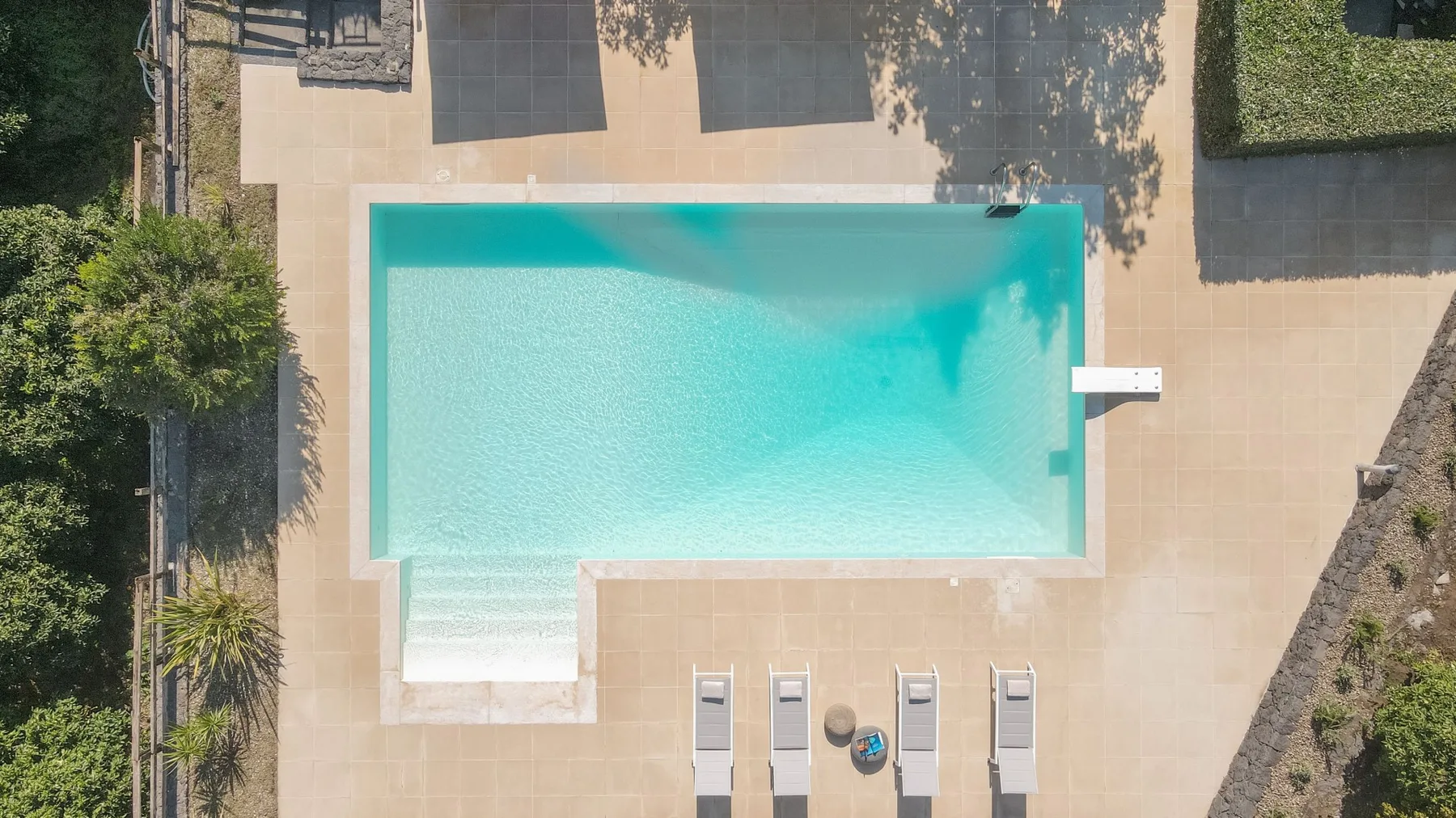 Una piscina al aire libre está rodeada por una terraza pavimentada y asientos.