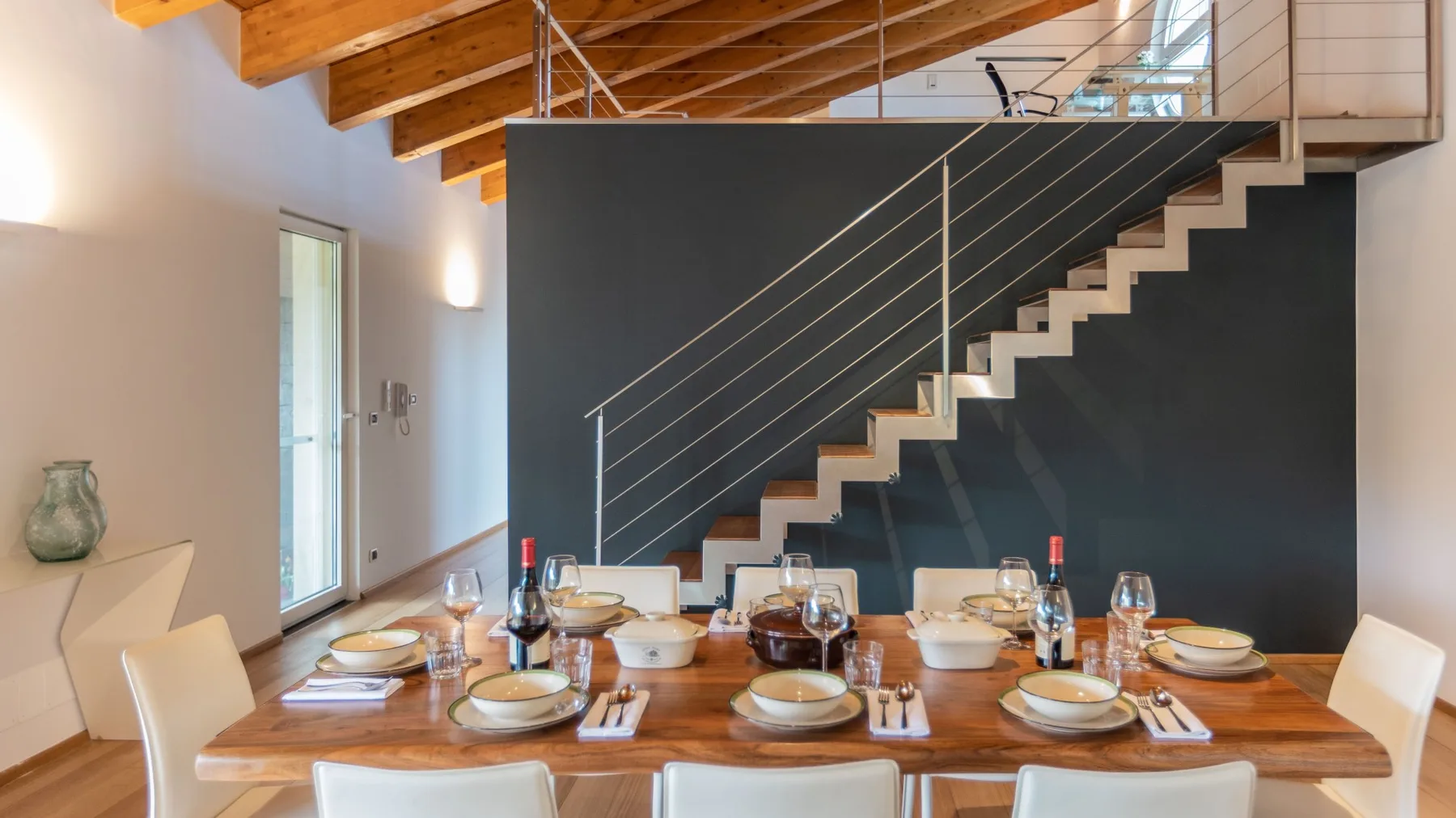 Comedor con la mesa puesta junto a una escalera y vigas de madera a la vista.