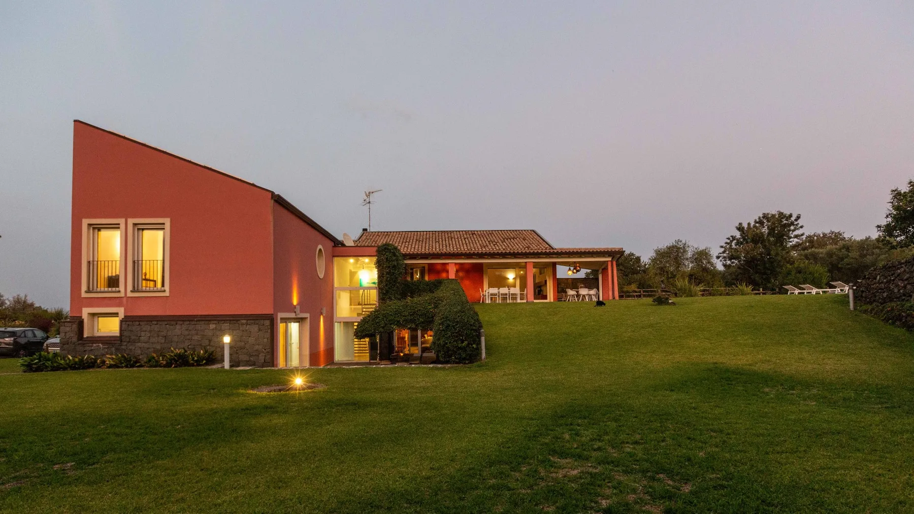 Una casa moderna de exterior rojo se encuentra junto a un amplio césped verde.