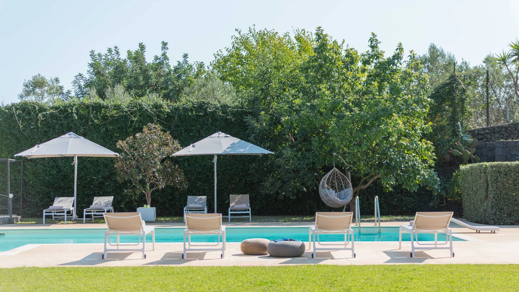 Una piscina al aire libre está rodeada de tumbonas y vegetación.