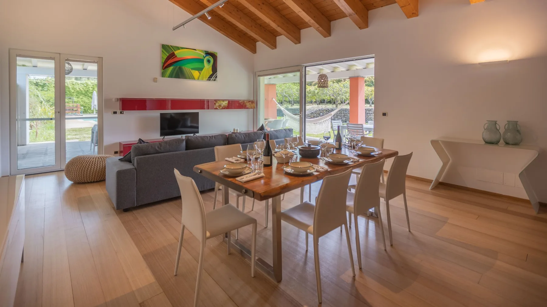 Una sala de estar y comedor diáfana con una mesa de madera y asientos grises.