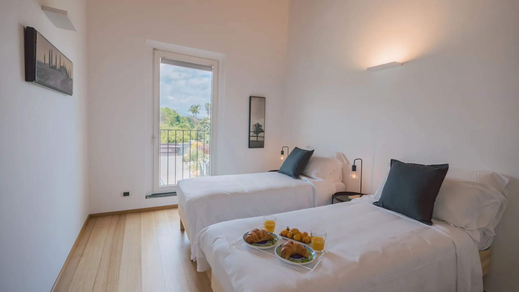 Un dormitorio luminoso con dos camas y un pequeño balcón visible por la ventana.