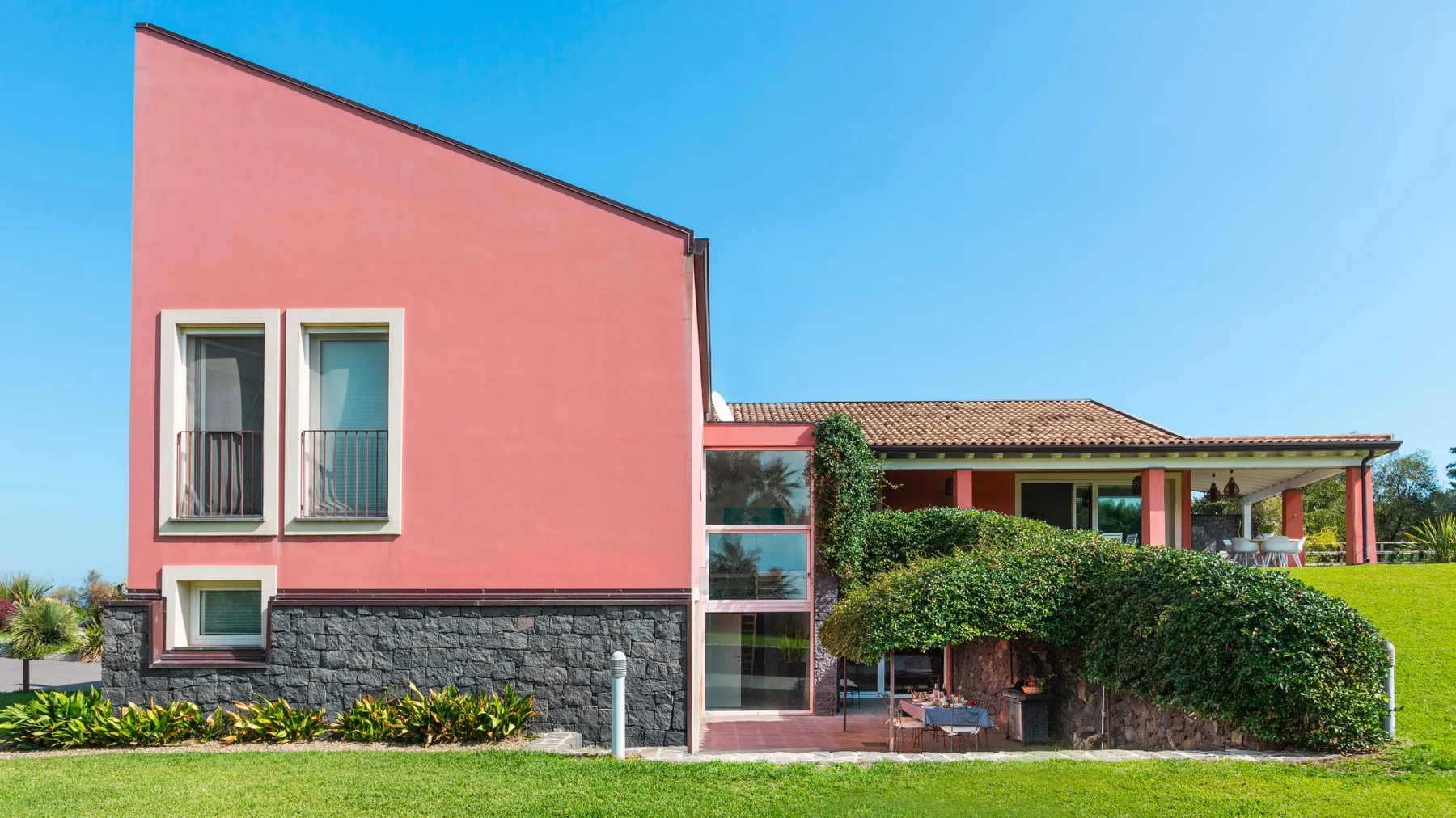 Una casa moderna con exterior rosa, ventanas y un patio cubierto.