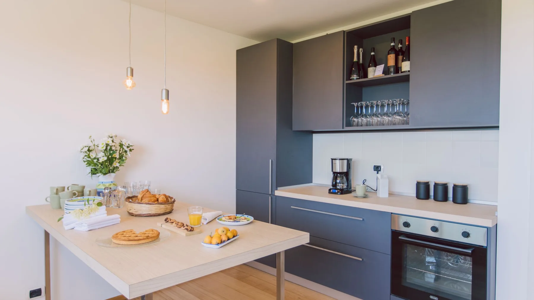 Una cocina moderna con gabinetes oscuros, un horno bajo la encimera y una mesa puesta con comida.