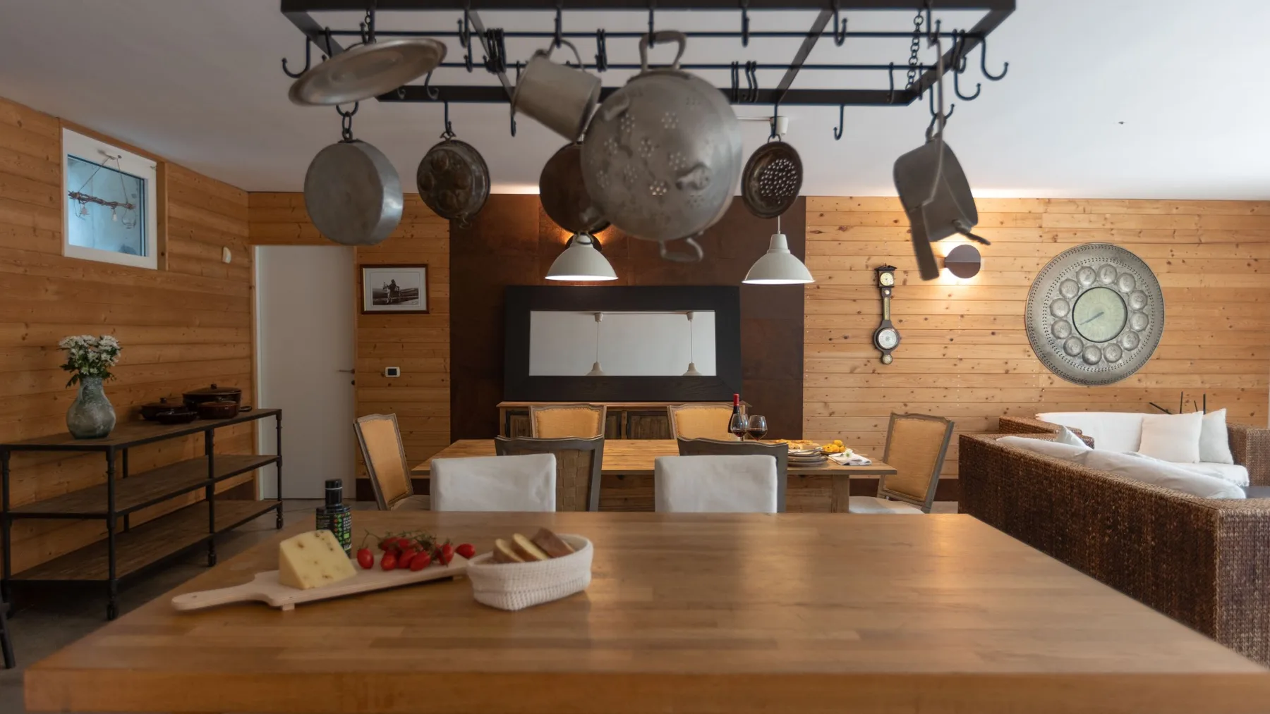 Comedor revestido de madera con una mesa grande y utensilios de cocina colgantes.