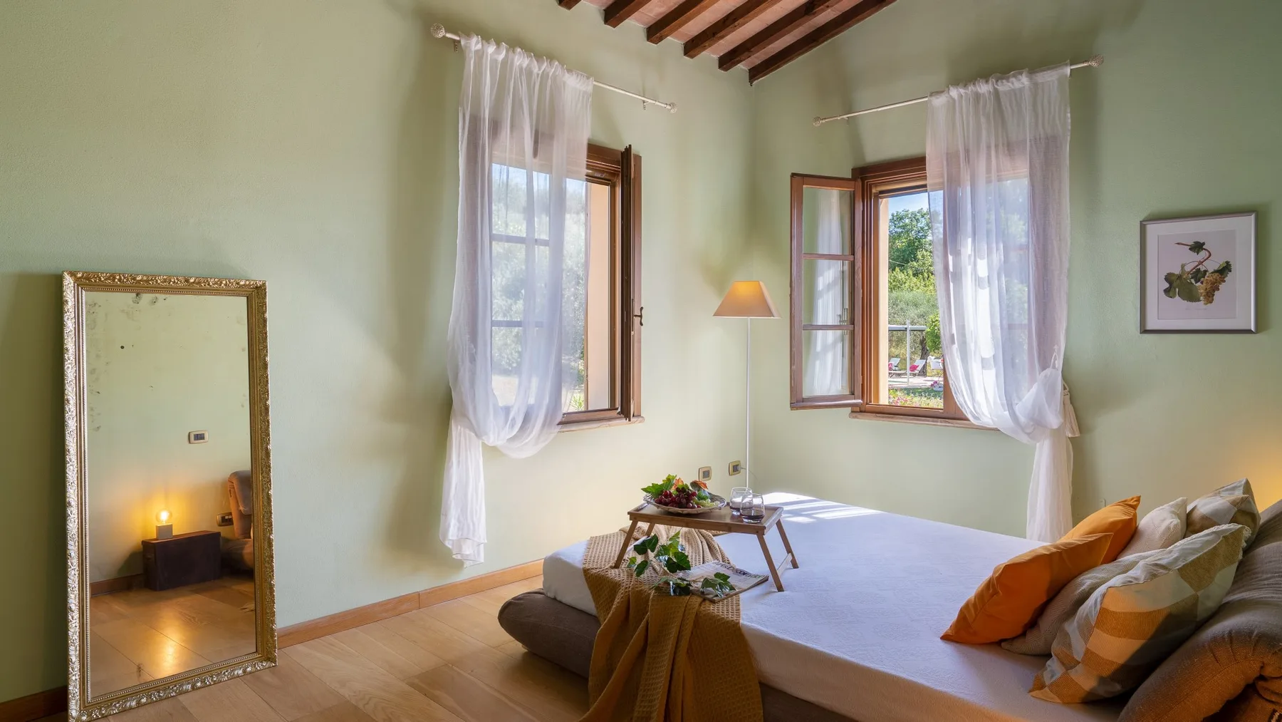 Un dormitorio con una cama baja, cortinas translúcidas y ventanas abiertas.