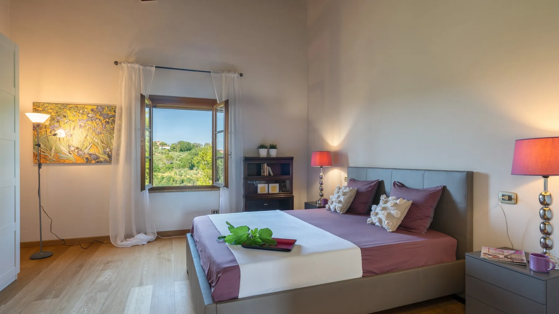 Un dormitorio con una cama grande, mesitas de noche y una ventana con vista a la vegetación.