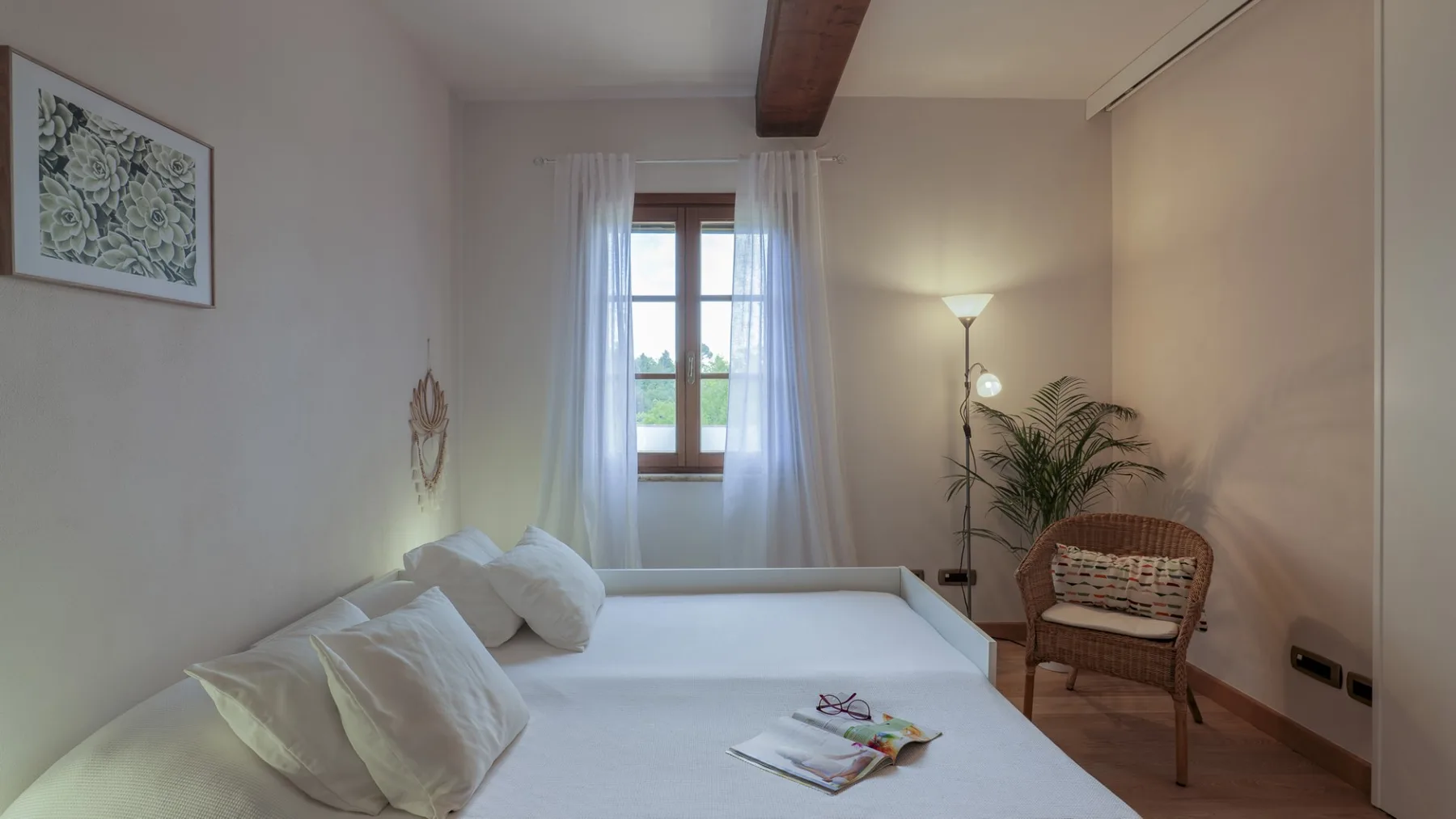 Un dormitorio con una cama, una ventana con cortinas y una silla de mimbre.