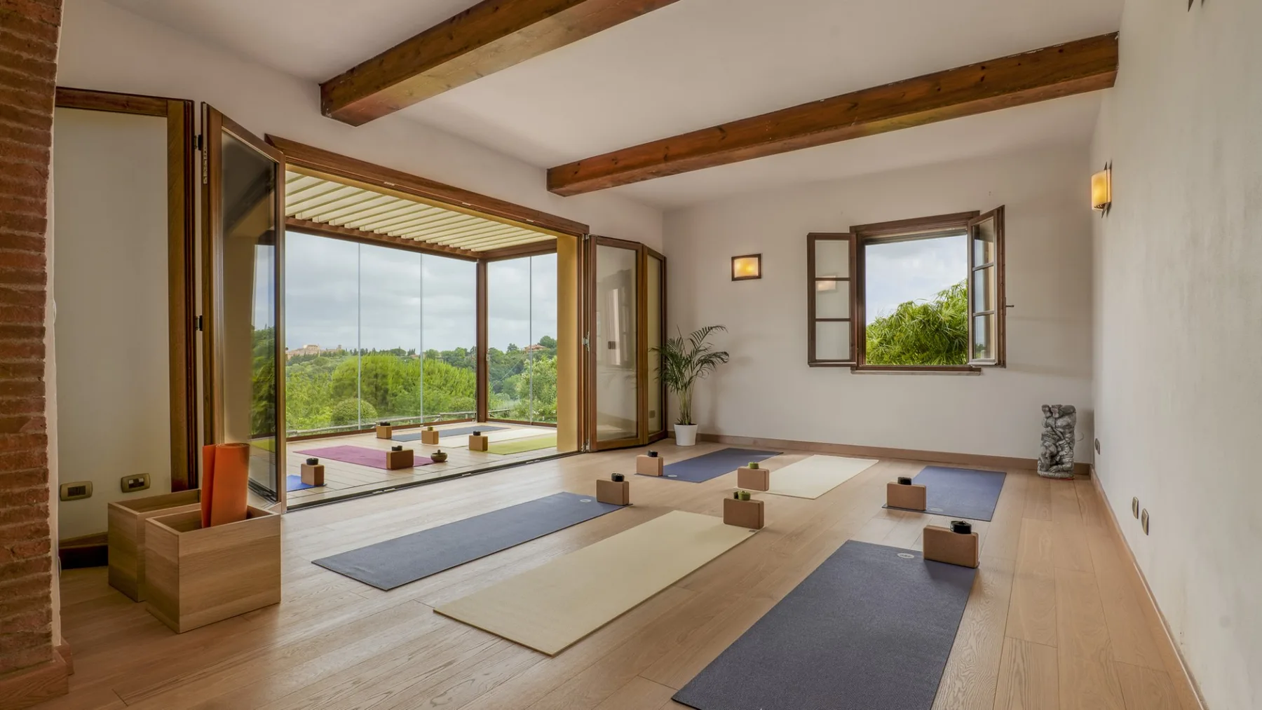 Una habitación luminosa con colchonetas y amplias ventanas con vista a la vegetación.