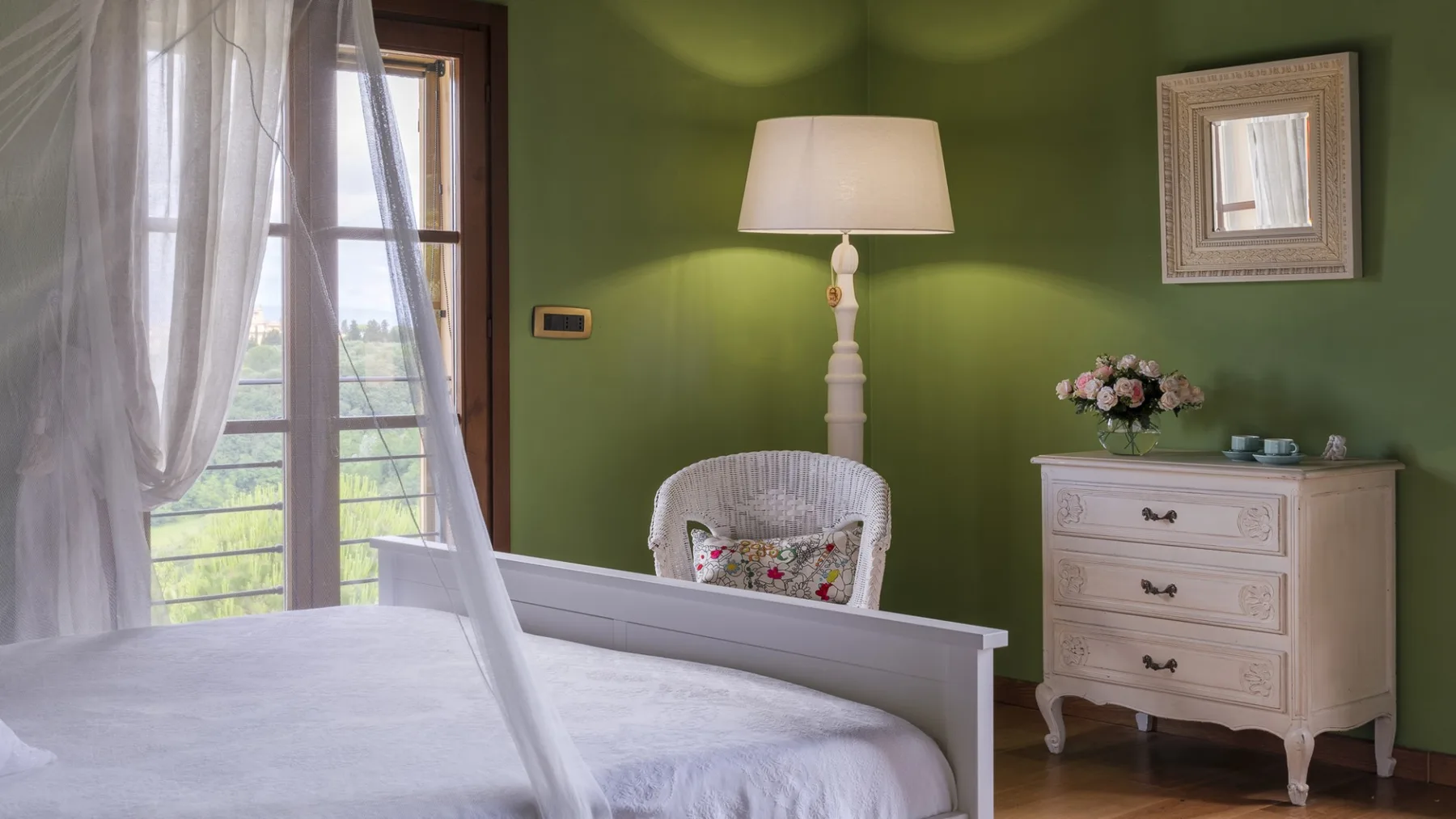Un dormitorio con una cama, una silla blanca y una lámpara de pie junto a paredes verdes.