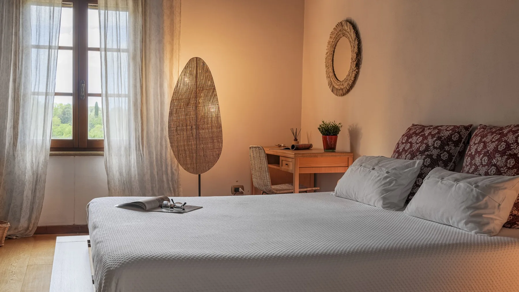 Un dormitorio con una cama bien arreglada junto a una ventana con cortinas.