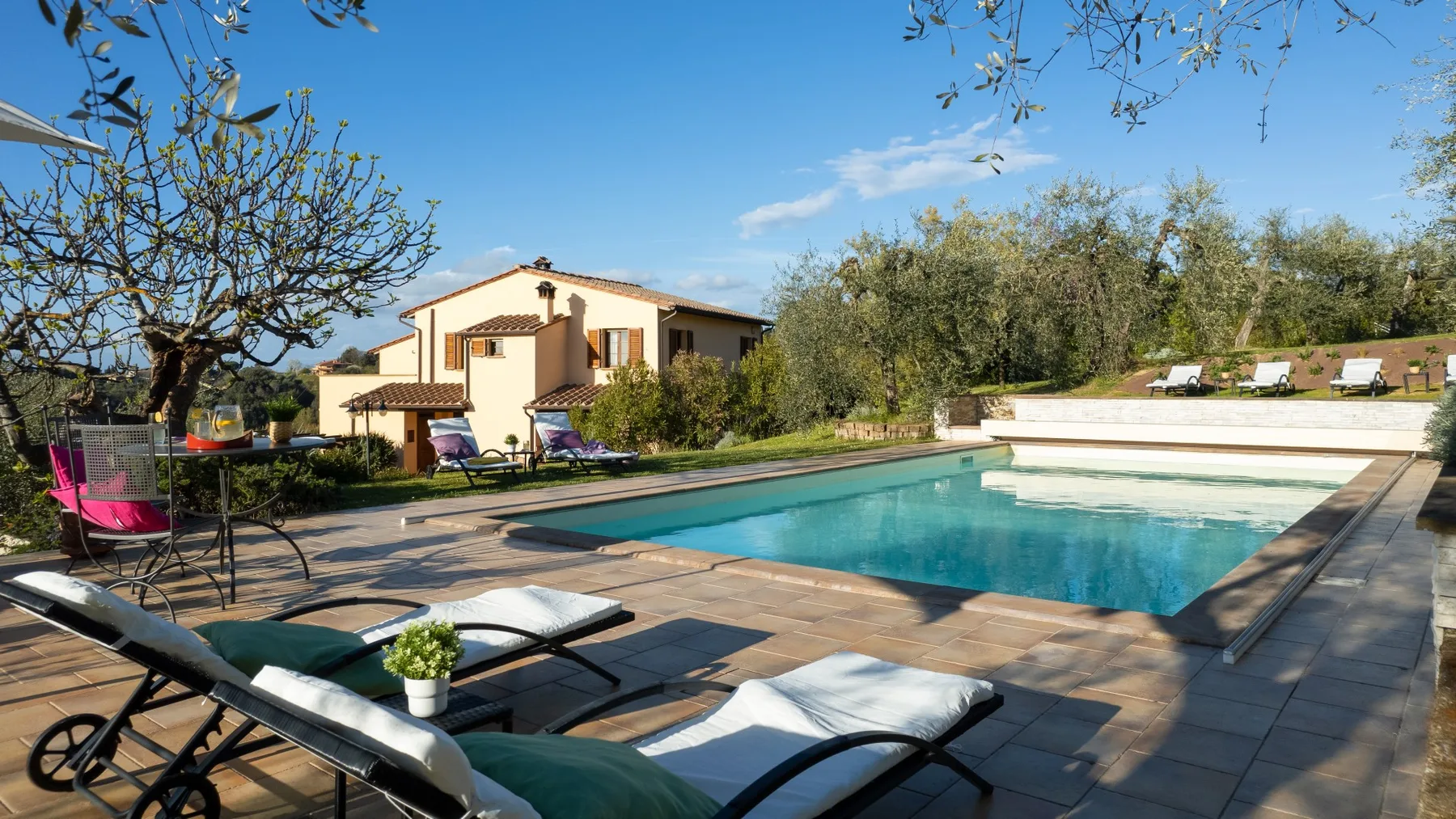 Una piscina junto a una casa, con asientos para descansar en el patio.