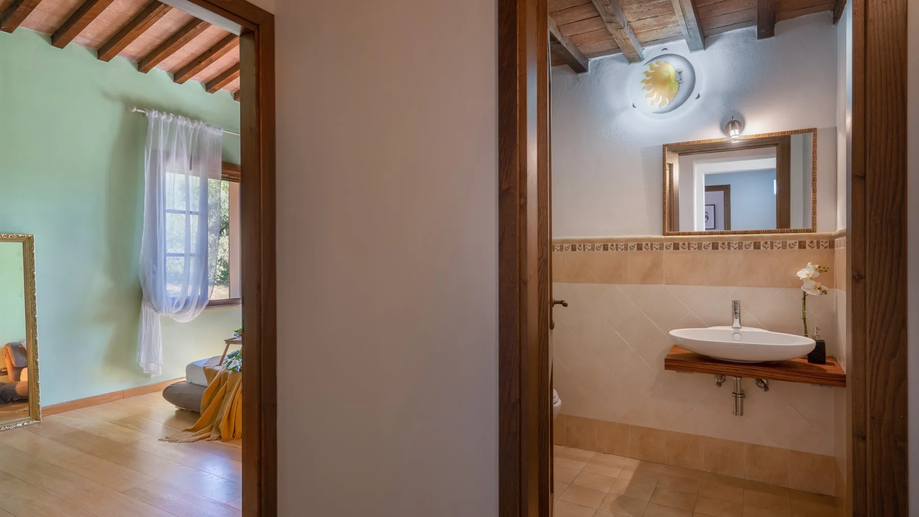 Un lavabo de baño con espejo en la pared y una puerta hacia una habitación contigua luminosa.