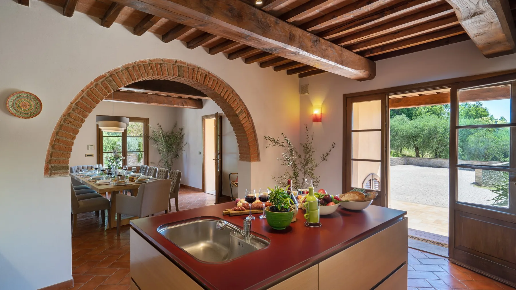 Una isla de cocina con fregadero y platos está junto a un comedor con arco.