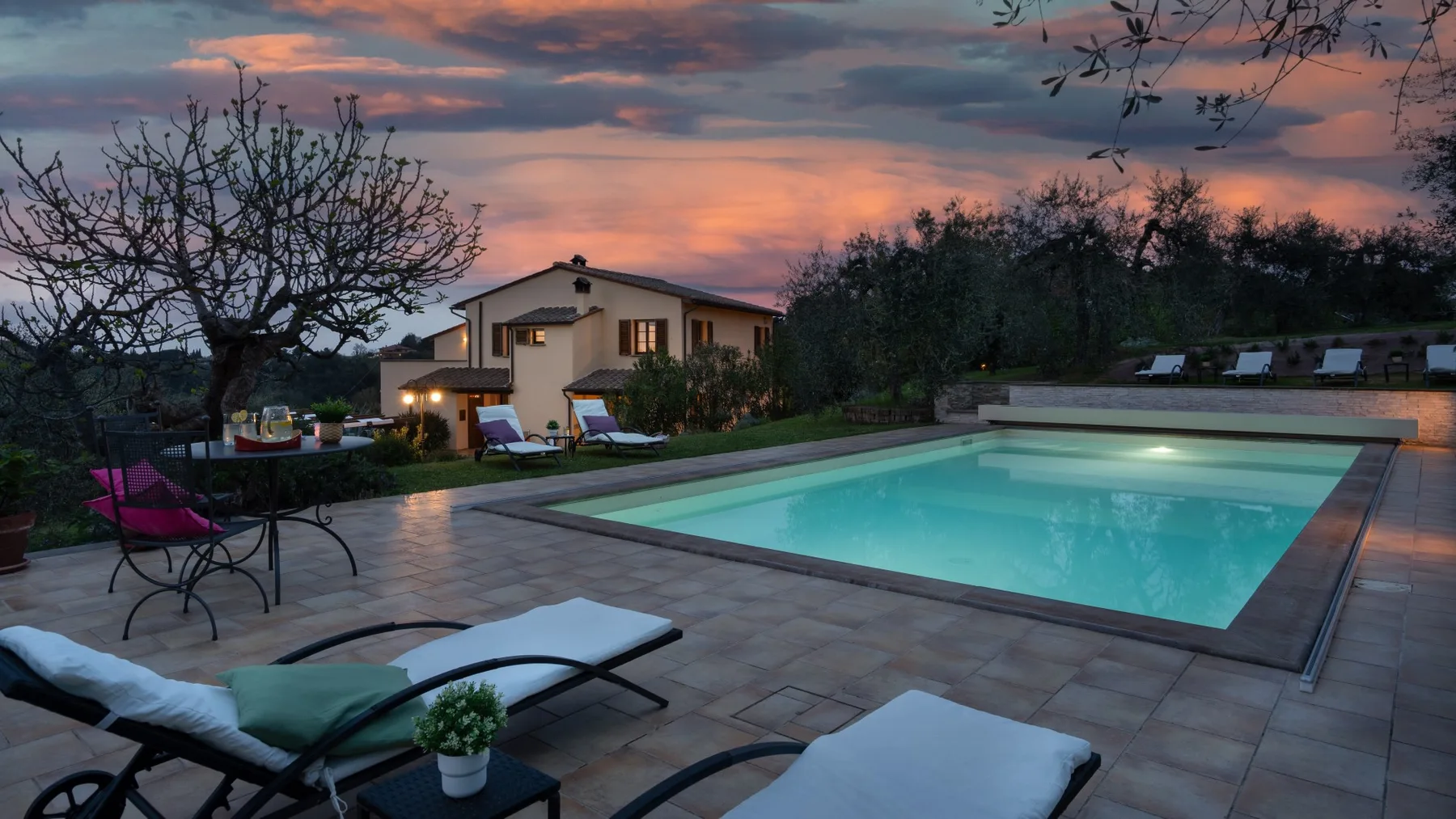 Una piscina y un patio están junto a una casa bajo un cielo colorido al atardecer.