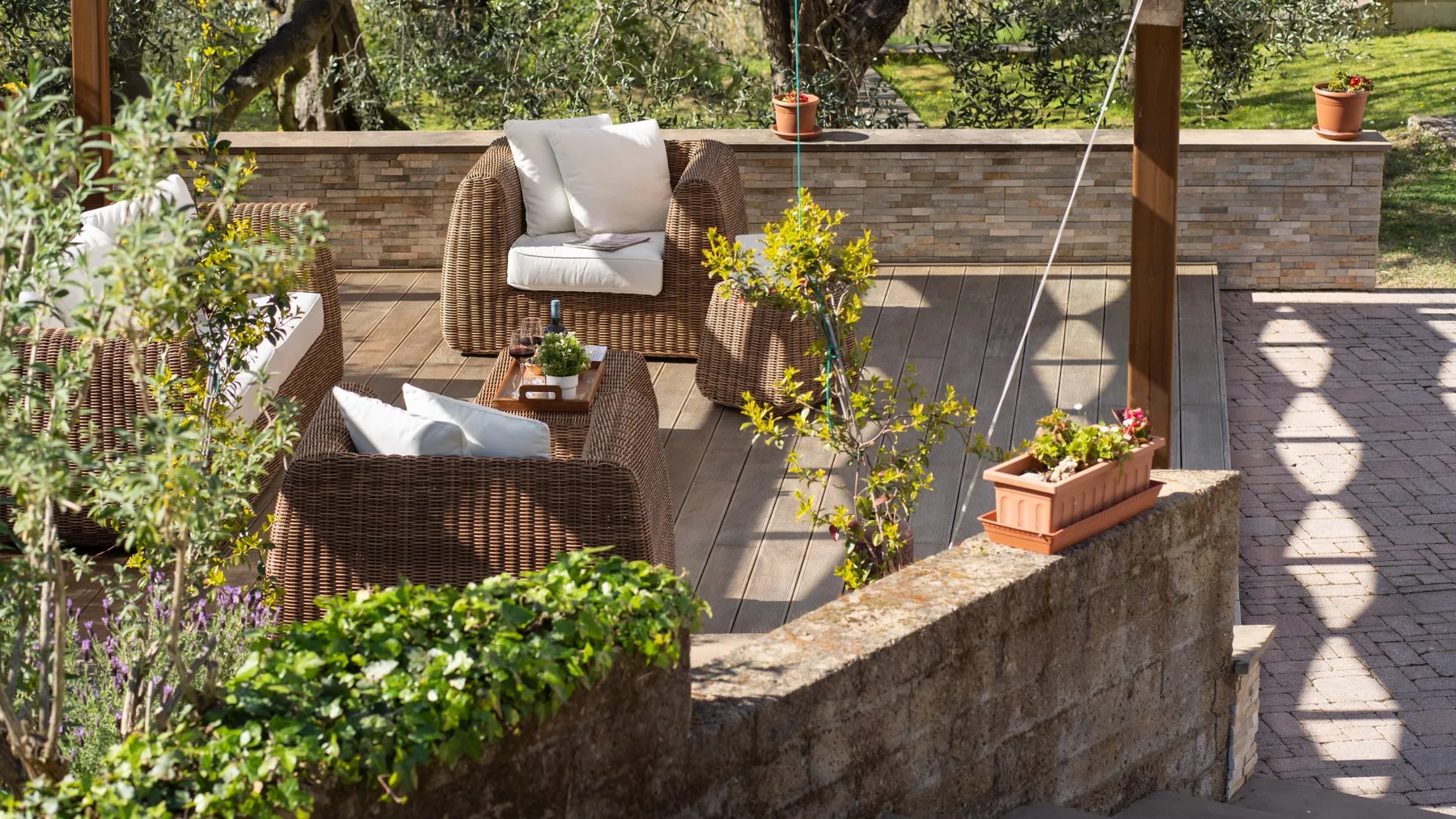 Un patio exterior pavimentado con asientos de mimbre y plantas frondosas.