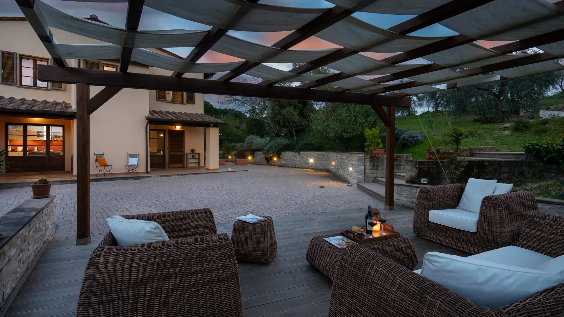 Una zona de estar exterior cubierta da a un patio pavimentado con luces cálidas.