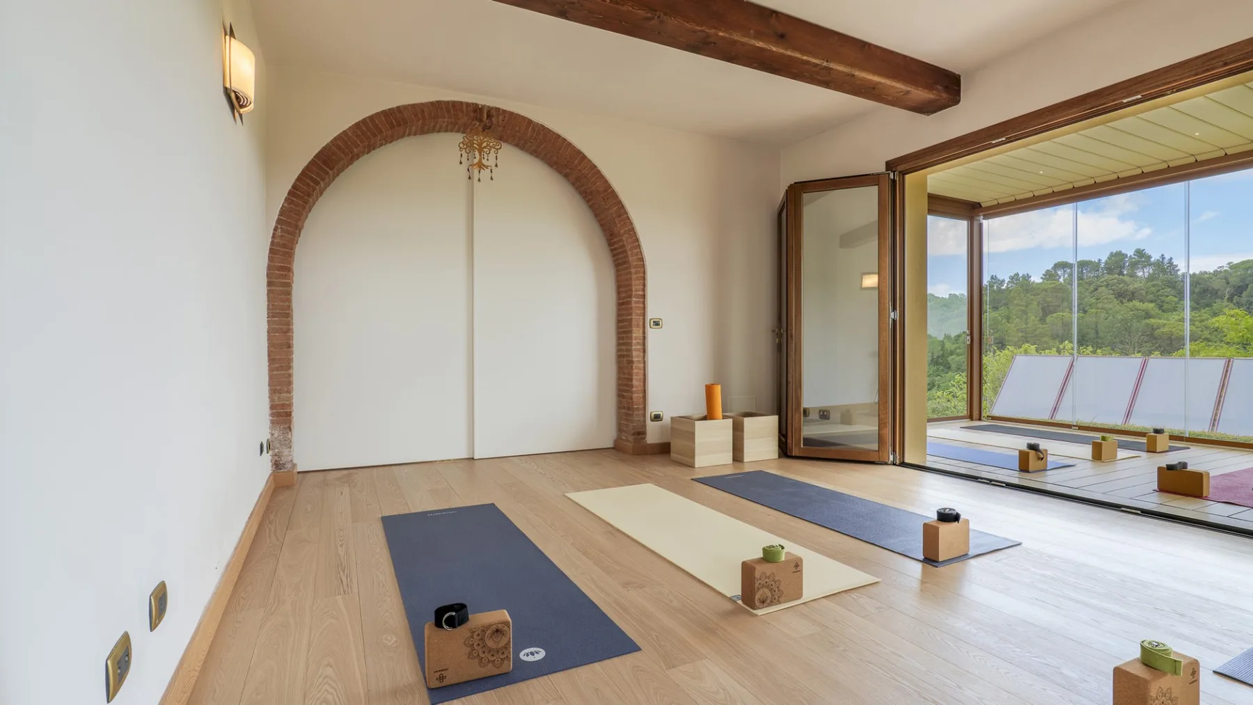 Un espacio interior luminoso con colchonetas y amplias ventanas con vistas a la vegetación.