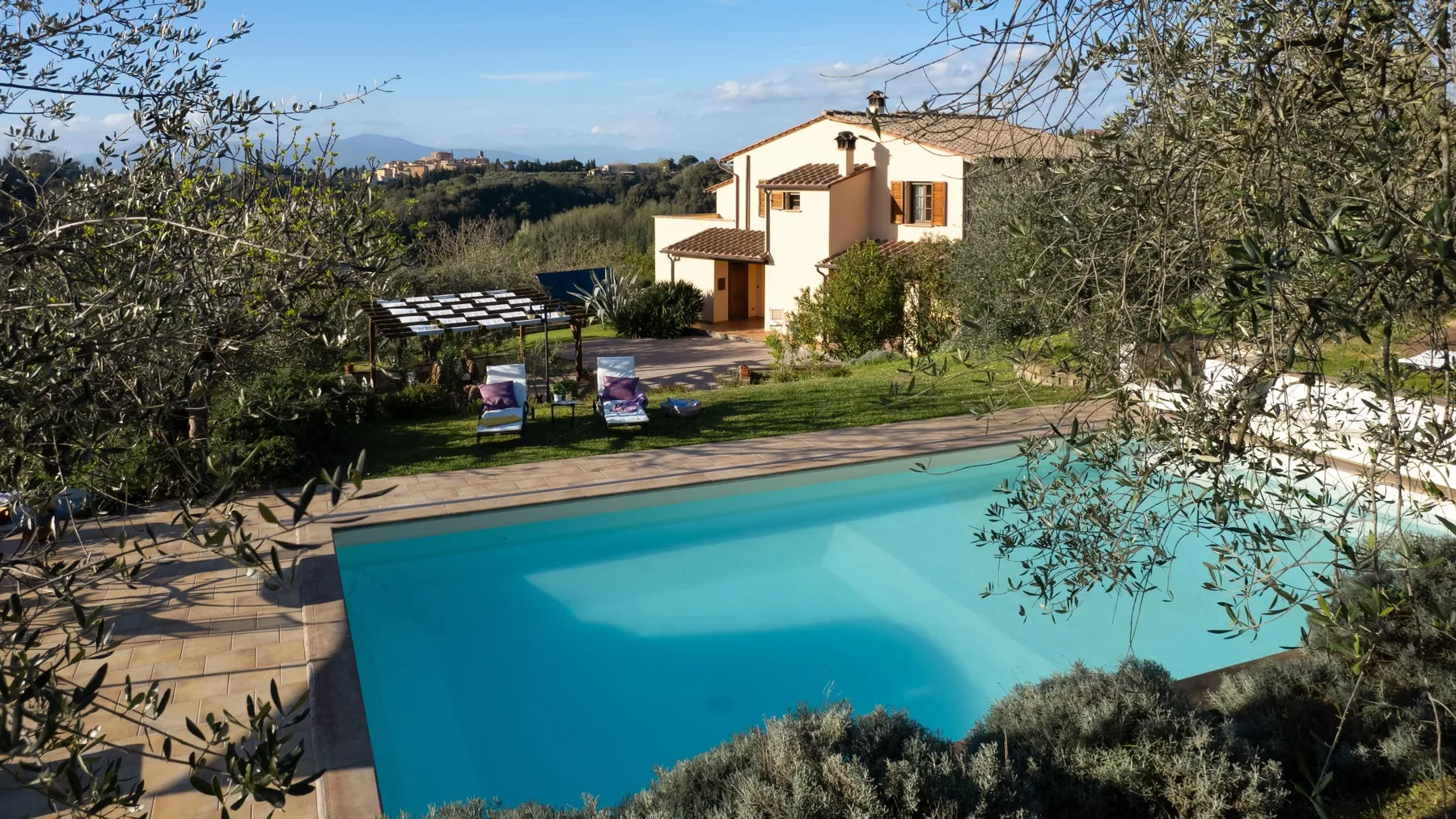 Una piscina al aire libre junto a un jardín y una casa de color claro.