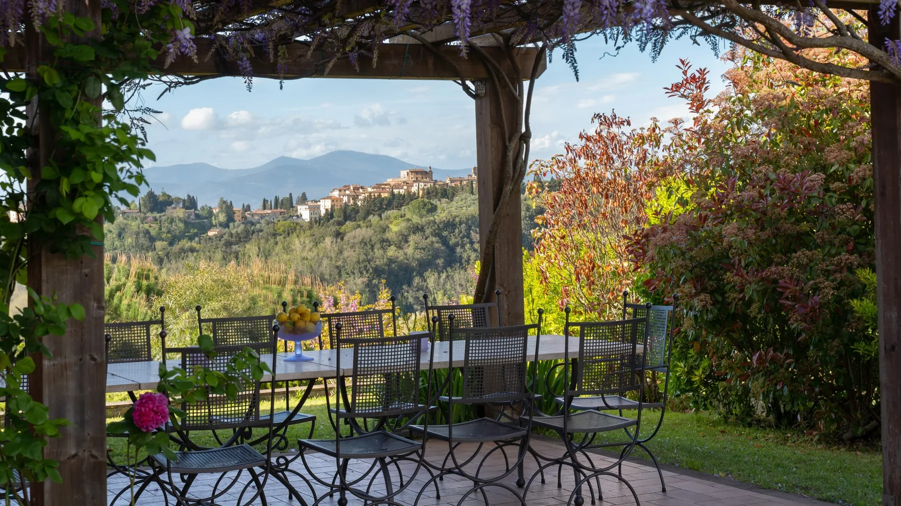 Un patio de jardín con asientos al aire libre da a un valle verde y colinas lejanas.