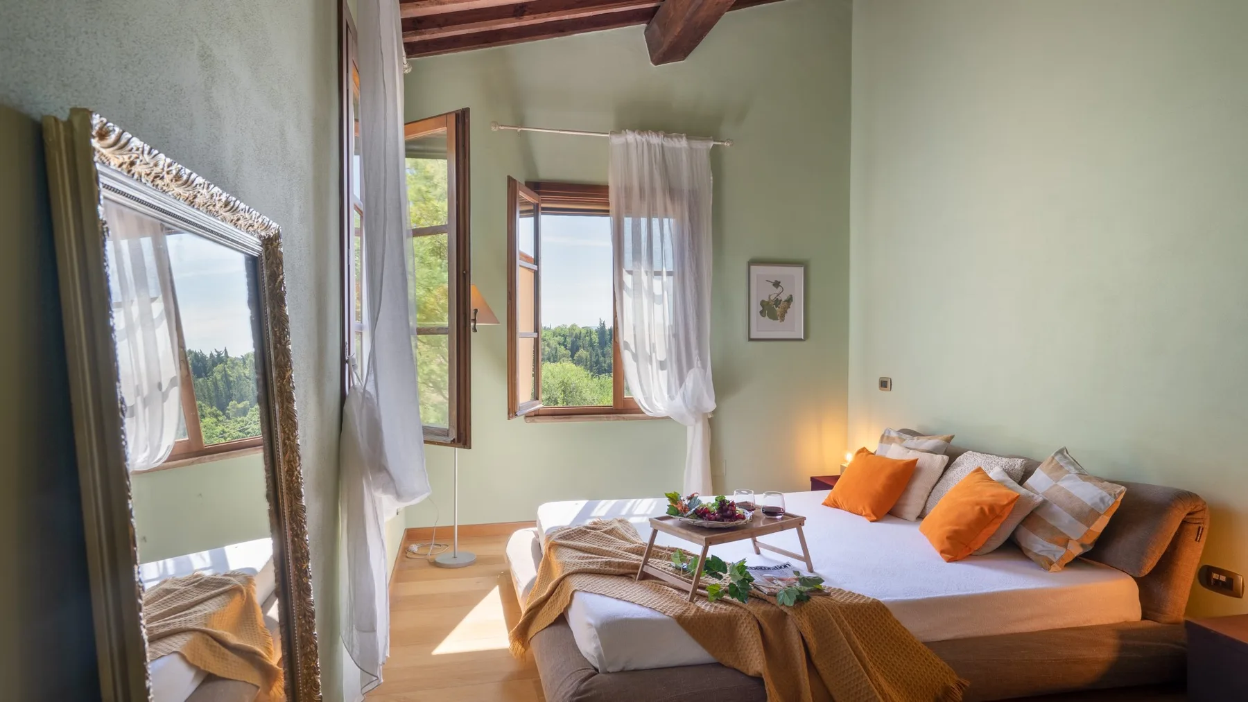 Un dormitorio con una cama adornada con cojines naranjas junto a ventanas abiertas.