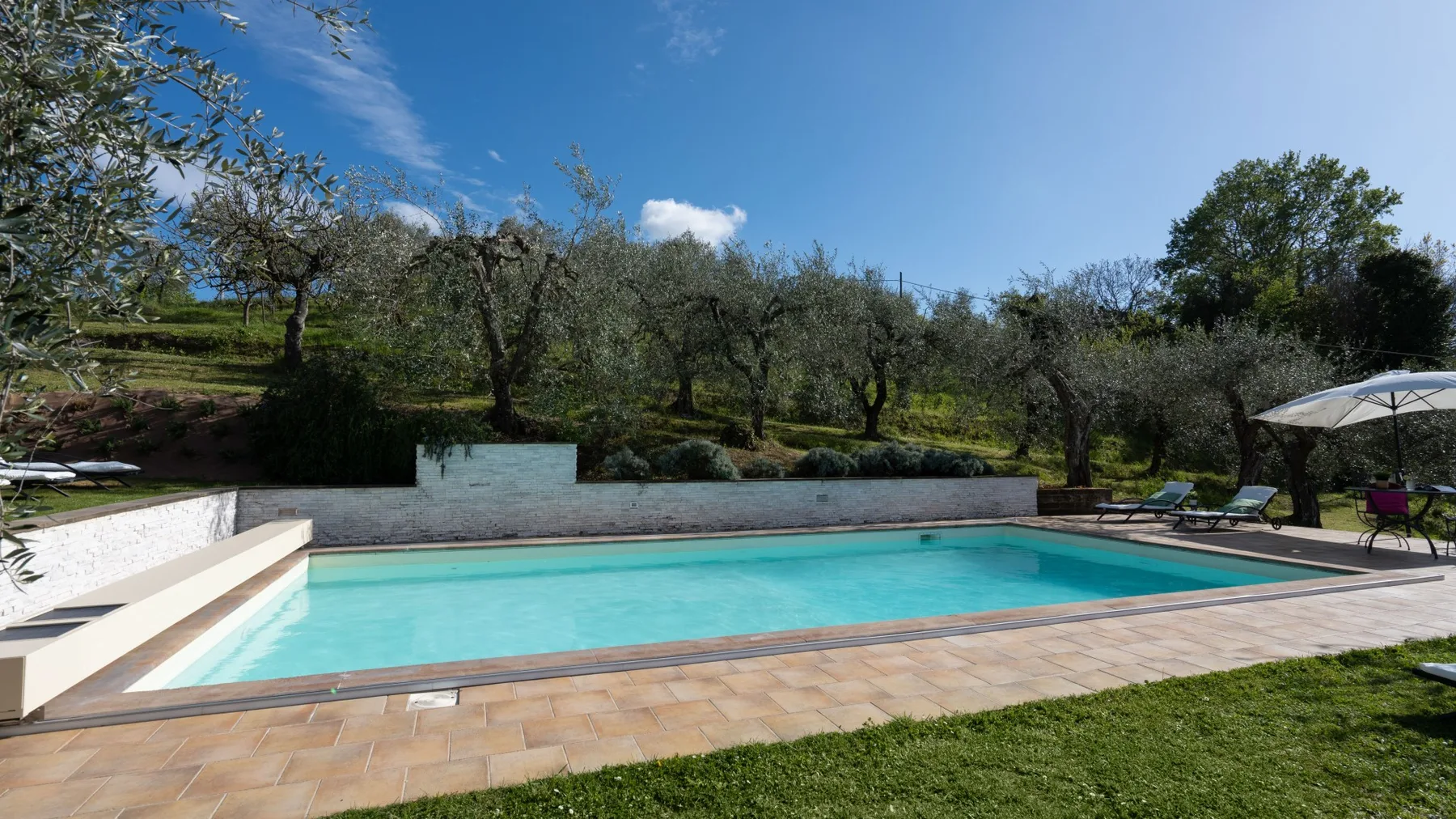 Una piscina al aire libre está rodeada por una terraza pavimentada y césped.