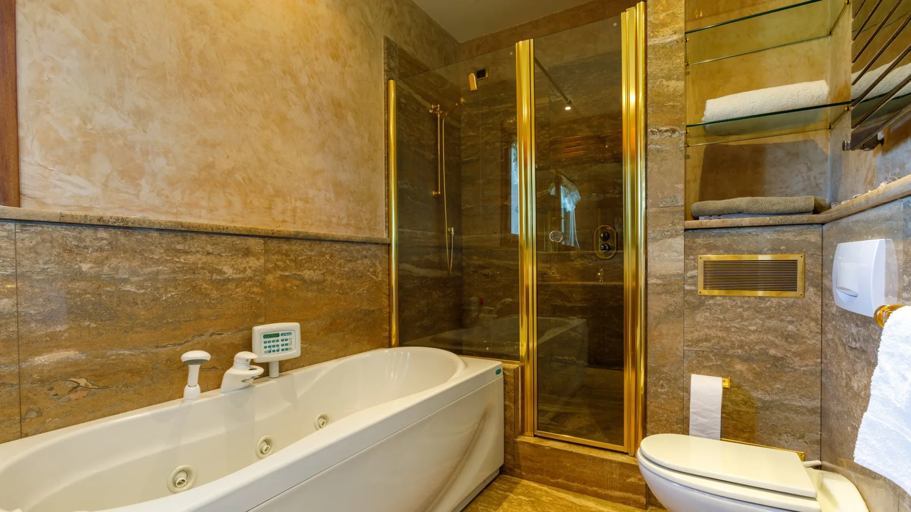 A bathroom with a built-in bathtub, glass shower enclosure, and toilet against stone-patterned walls.
