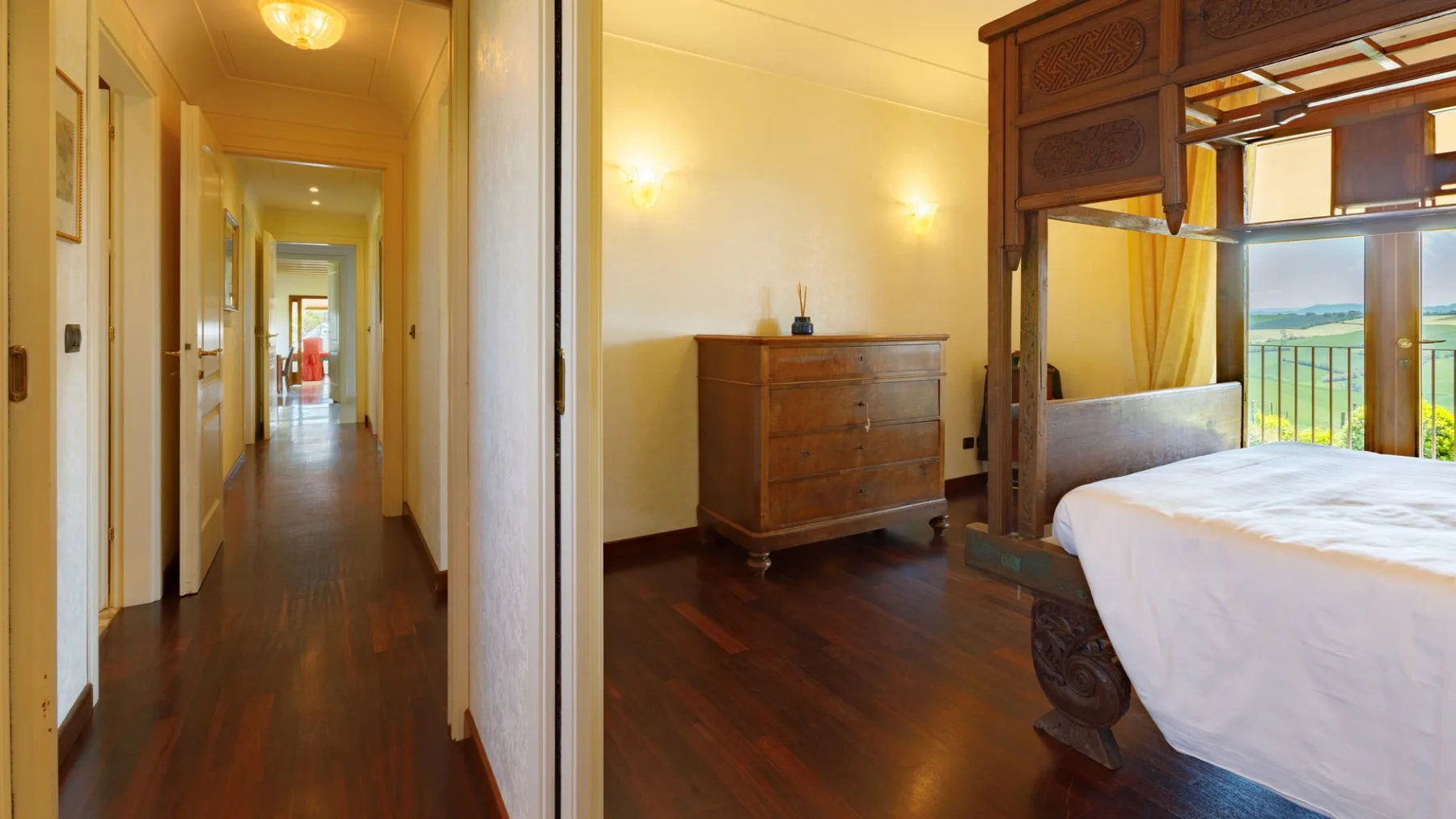 A bedroom with a dark wooden four-poster bed, white bedding, a dresser, and a hallway.