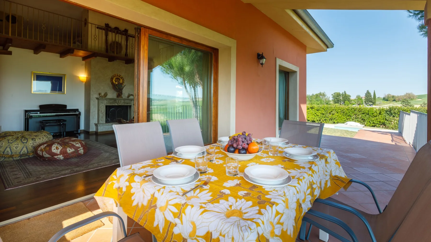A sunny patio dining table is set with dishes and fruit beside a sliding glass door.