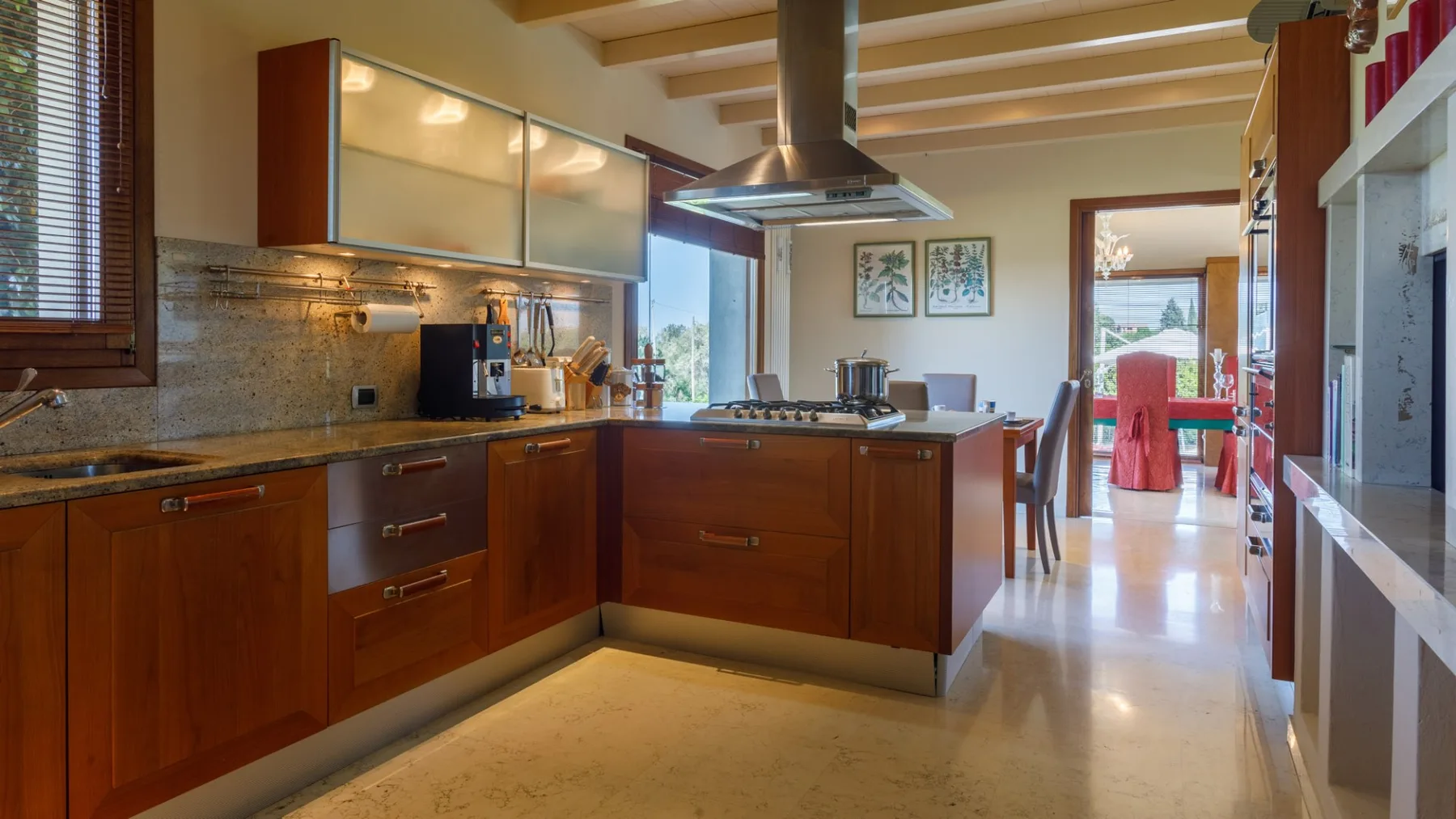 A spacious kitchen with reddish wood cabinets, a central island, and a stainless steel range hood.