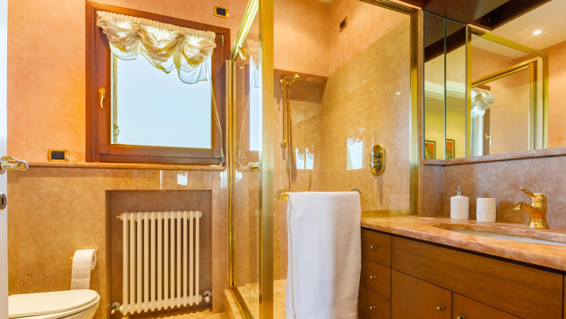 A warm-toned bathroom has a bathtub, radiator, mirrored vanity, and a towel hanging beside the counter.