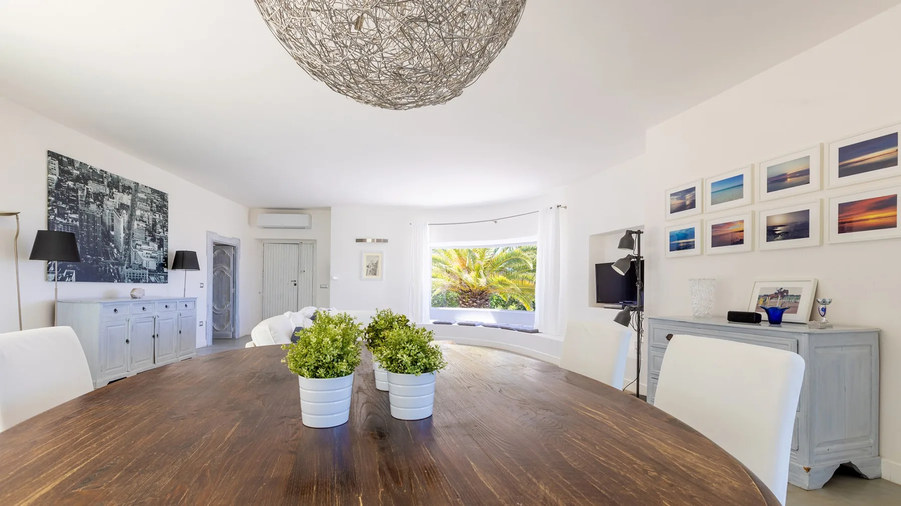 Un comedor luminoso con una mesa grande de madera y cuadros en la pared.