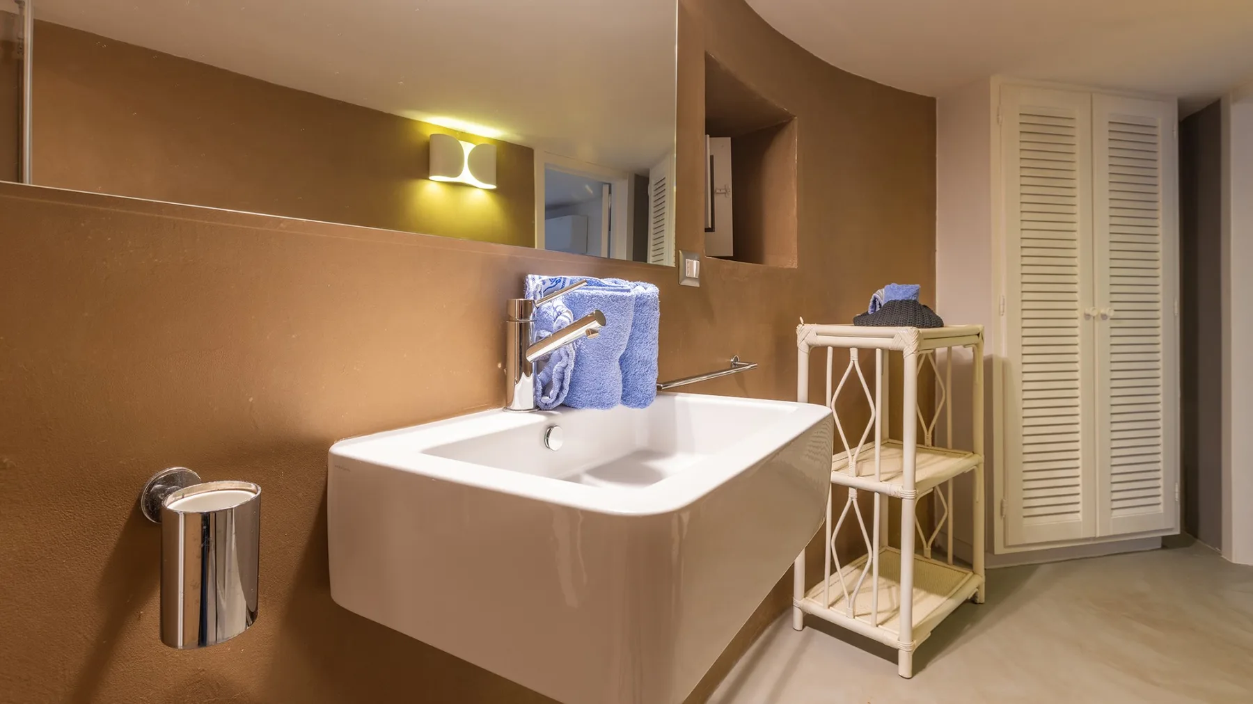 Un baño con un lavabo suspendido y un pequeño estante de almacenamiento al lado.