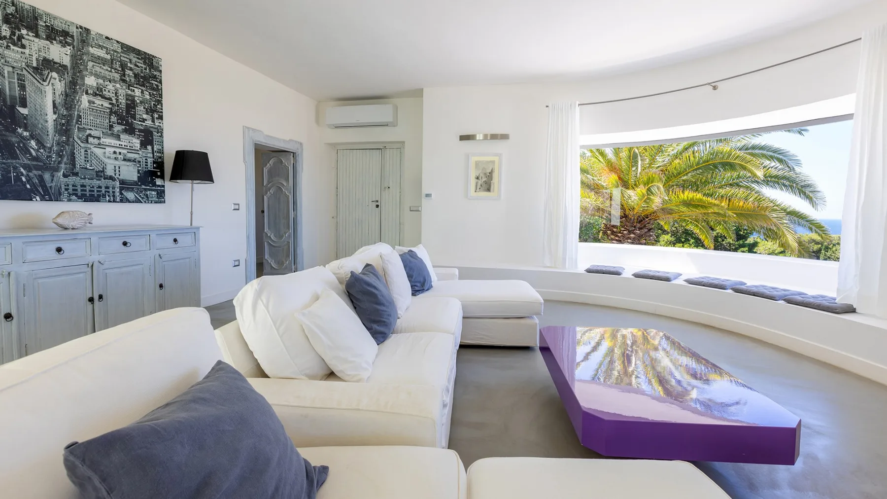 Una sala luminosa con asientos blancos y una gran ventana con vista a palmeras.