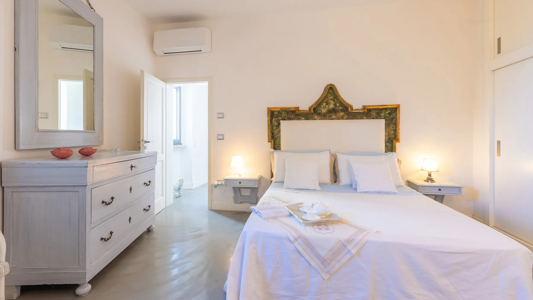 Un dormitorio con una cama bien tendida y una cómoda junto a la puerta.