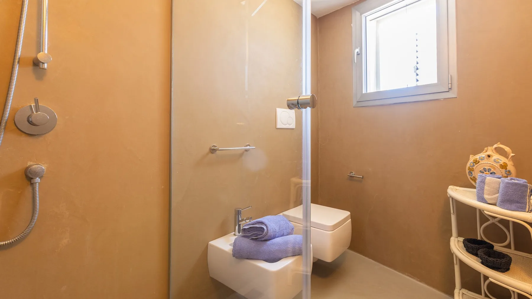 Un baño con ducha de vidrio, inodoro y una ventana pequeña.