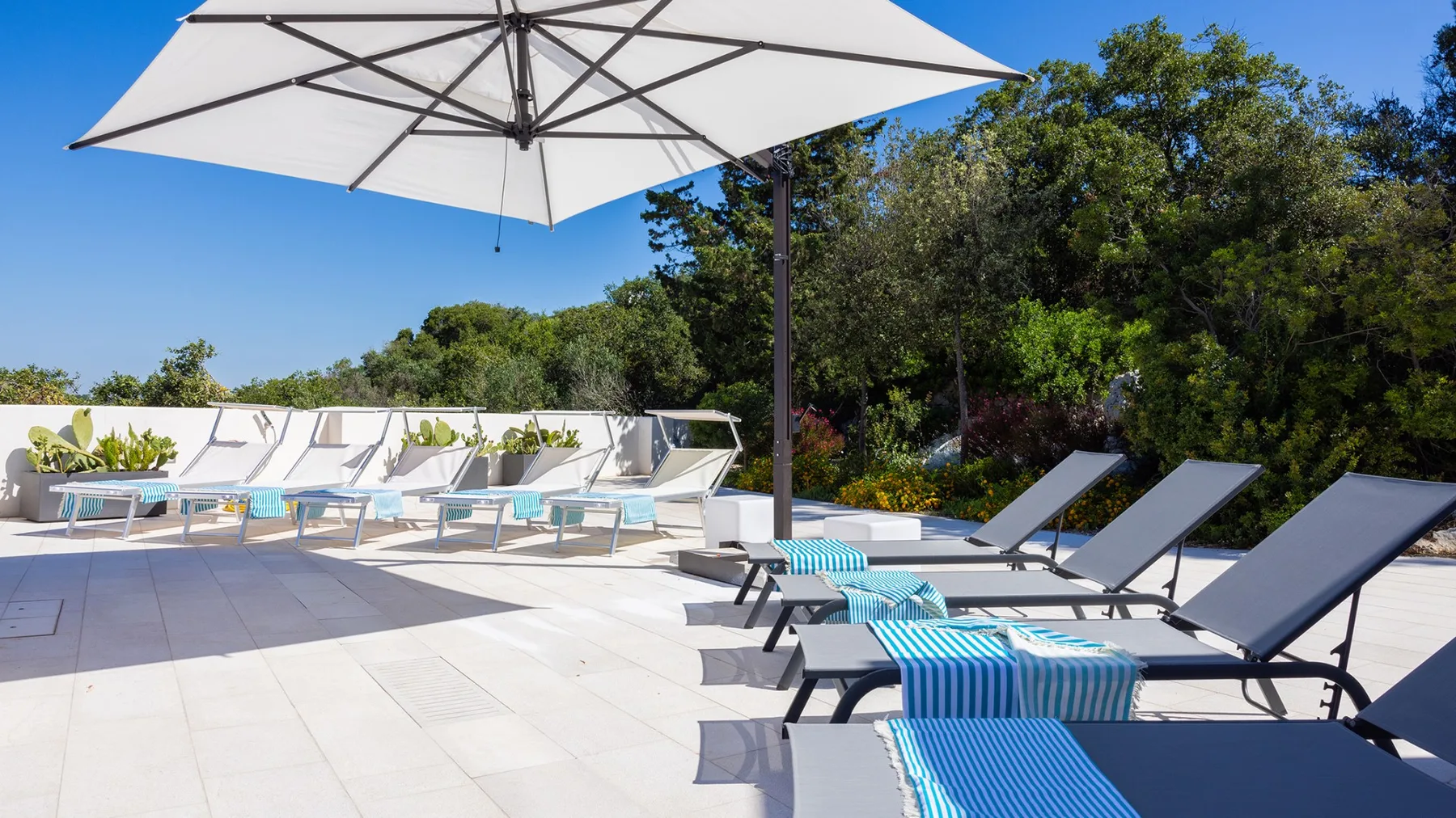 Un patio soleado junto a la piscina tiene tumbonas bajo una gran sombrilla.