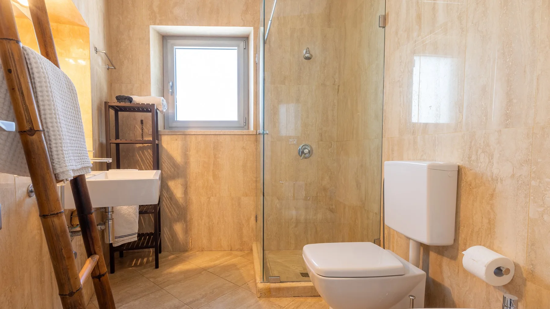 Un baño con ducha de cristal, inodoro y una ventana pequeña.