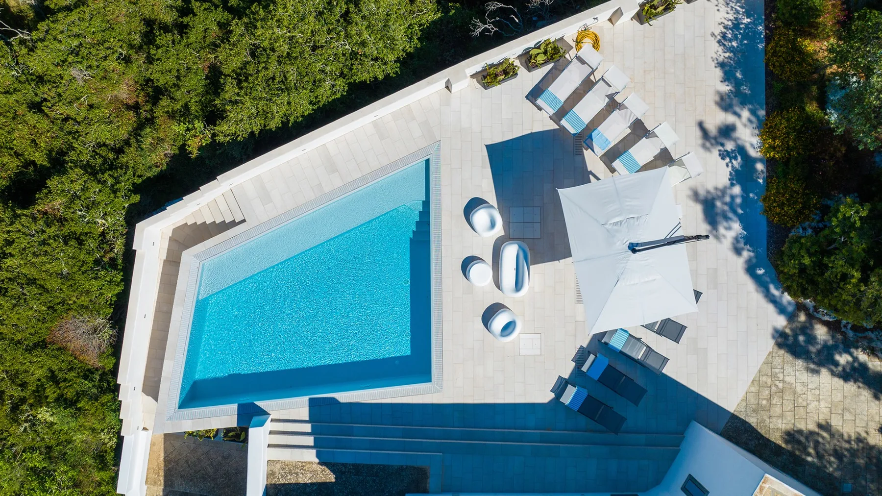 Vista aérea de una piscina junto a un patio pavimentado con asientos reclinables.