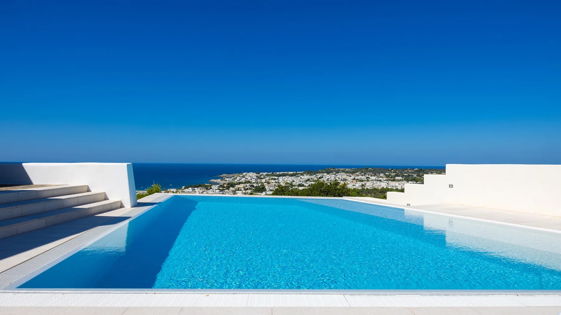 Una piscina al aire libre tiene vistas al mar y a un asentamiento costero.