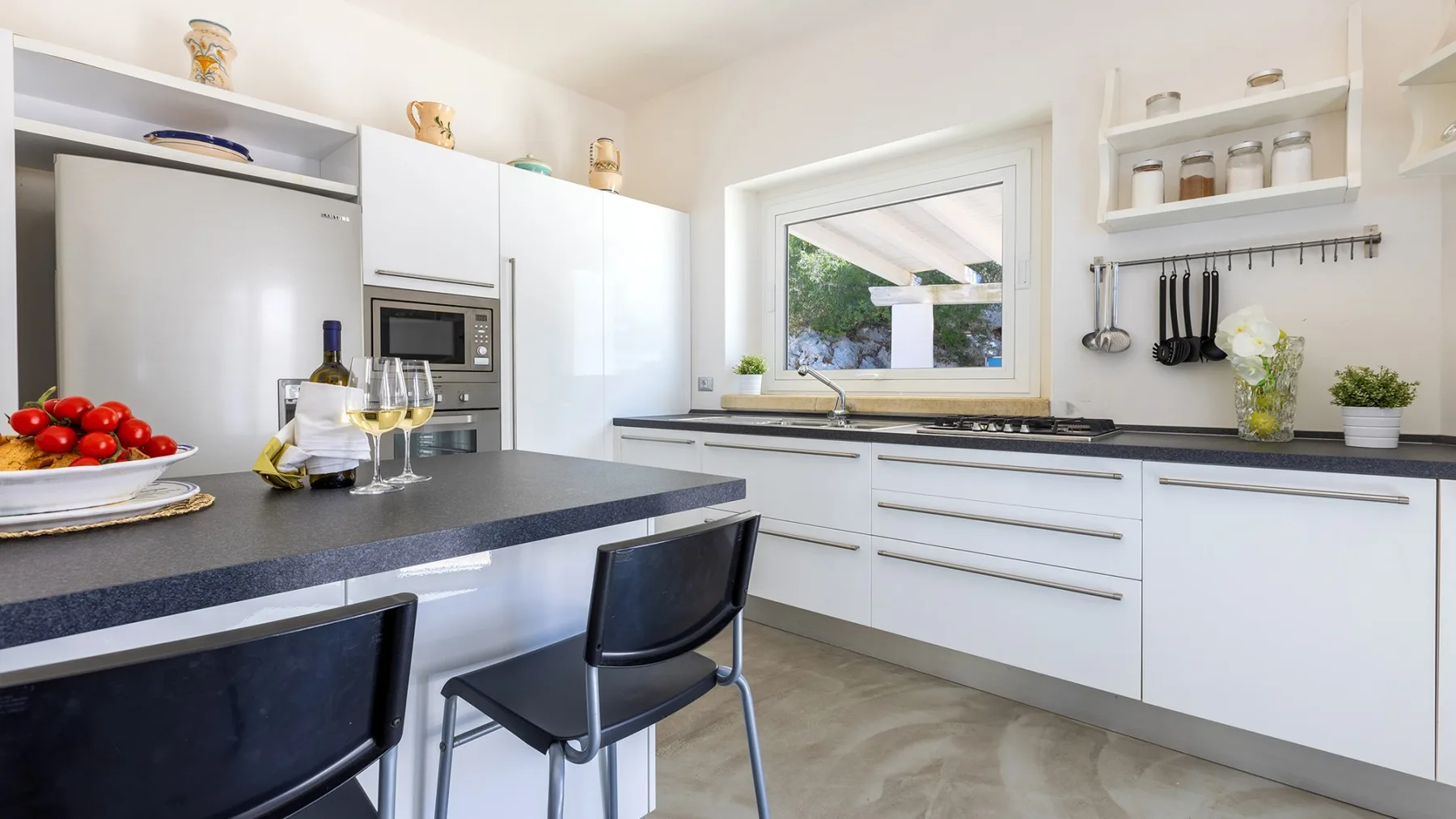 Una cocina luminosa con gabinetes blancos, encimeras oscuras y una ventana sobre el fregadero.
