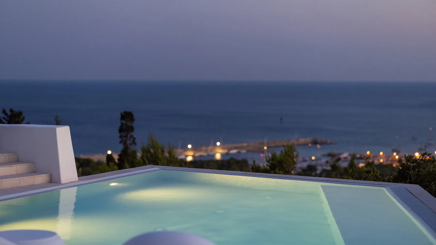 Una piscina iluminada mira al mar al anochecer.