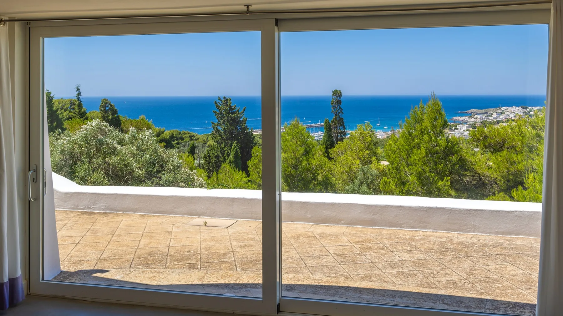 Una vista al mar a través de puertas corredizas de vidrio da a una terraza embaldosada.
