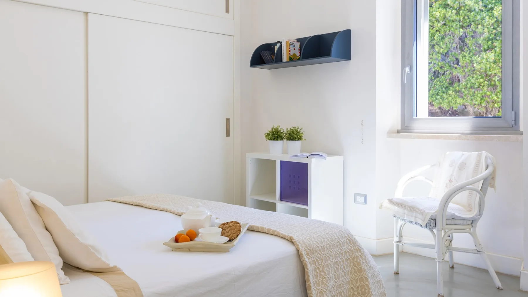 Un dormitorio luminoso con una cama, una silla blanca y una ventana grande.