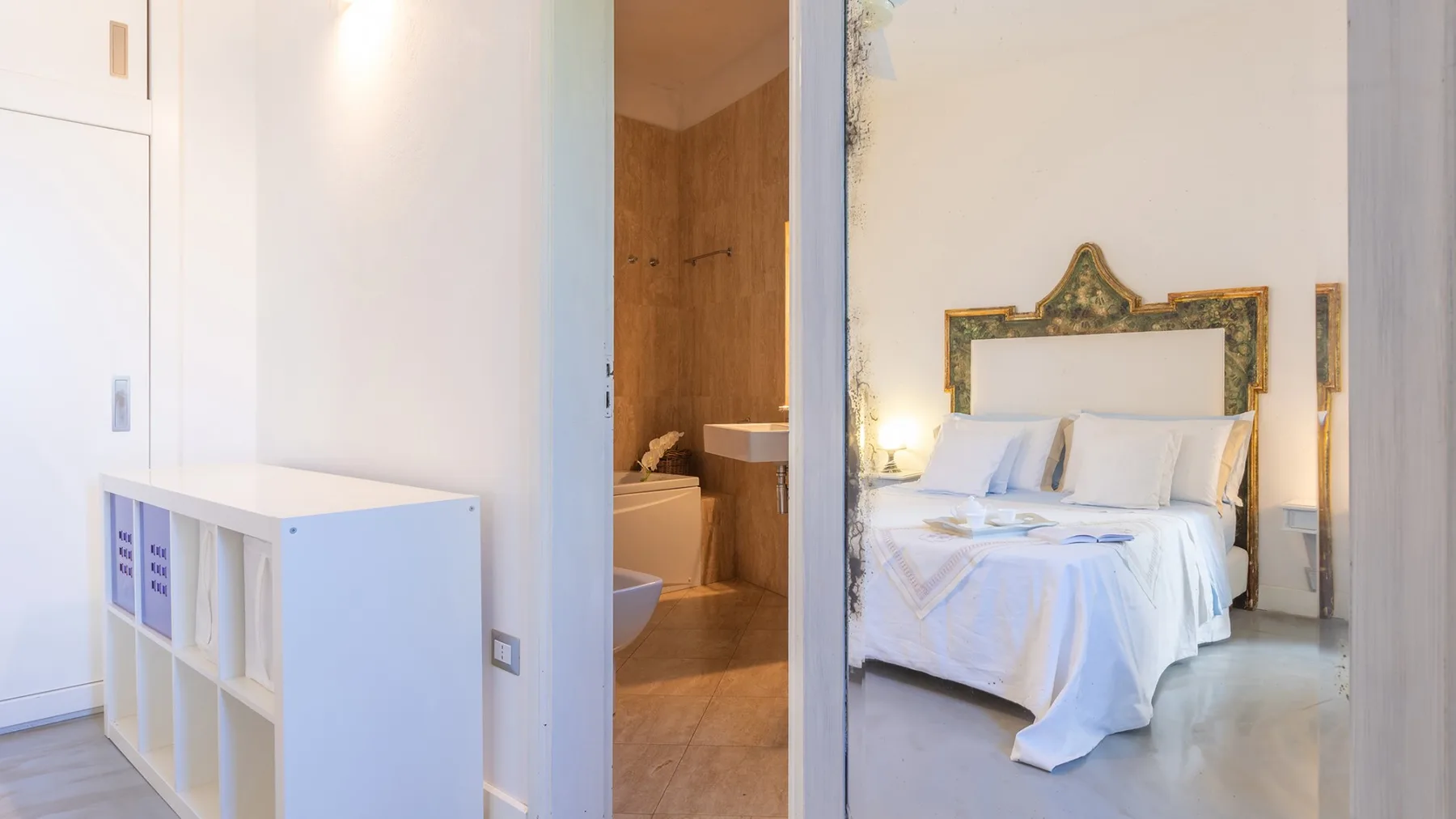 Un dormitorio con una cama ordenada junto a la entrada abierta de un baño.