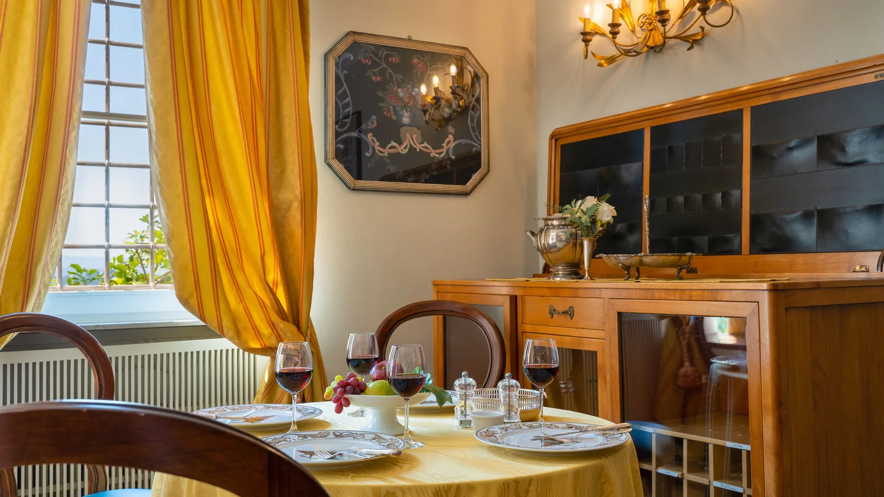 A dining room with a set table beside a tall window with golden curtains.